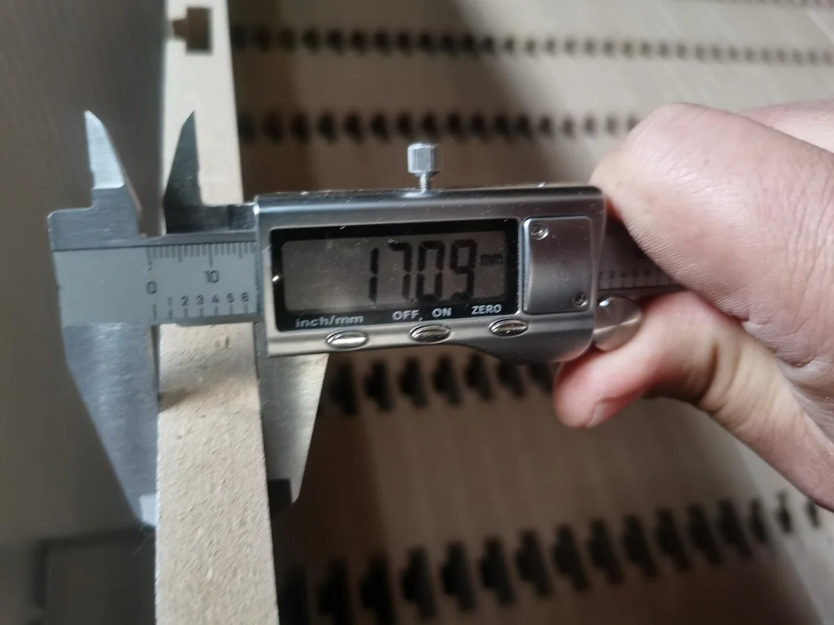 Digital caliper reading 17.09 mm on the white slotted MDF panel