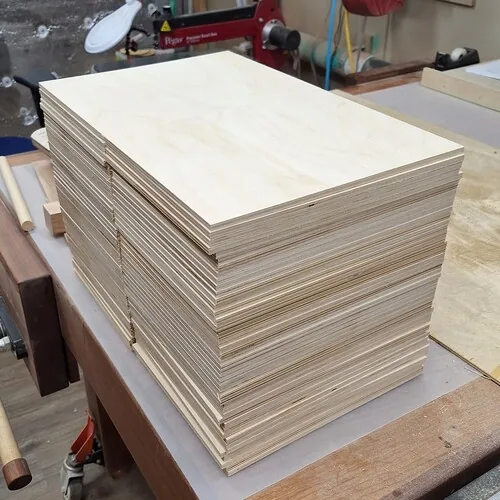 Pale plywood sheets stacked on a workbench, with thin layered edges visible.